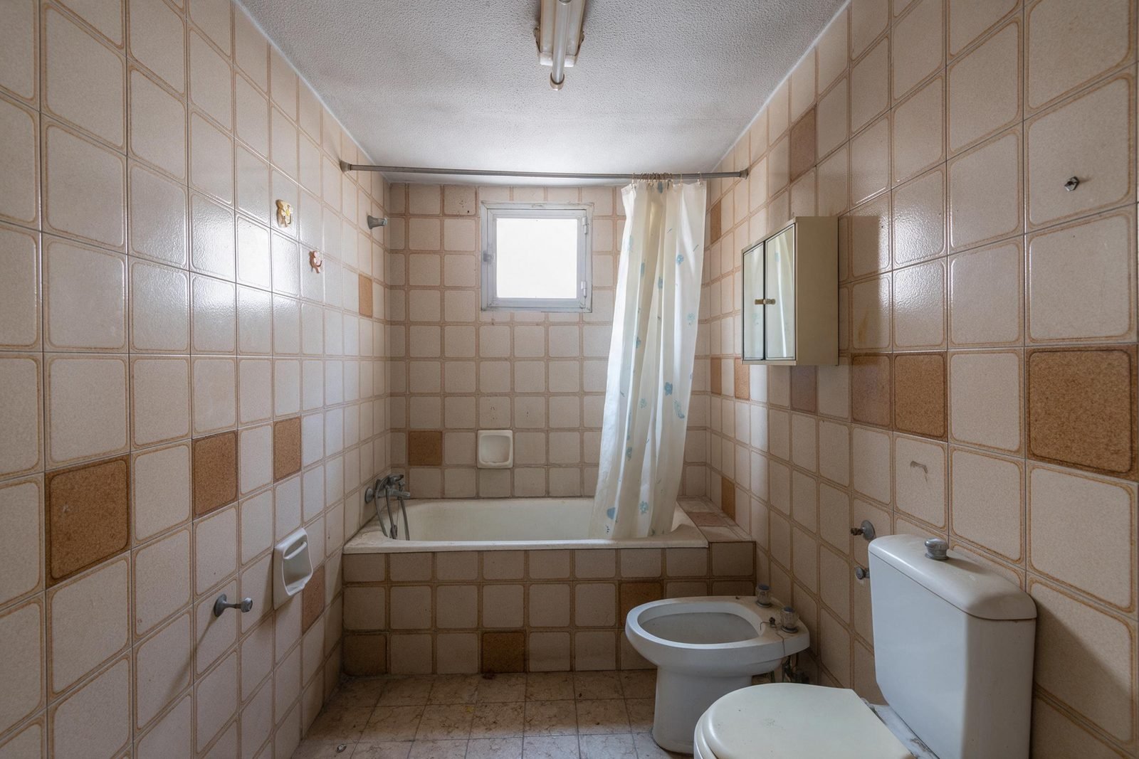 Baño antiguo de piso madrileño con bañera alta, azulejo de los años setenta y grifería desgastada, antes de reformar