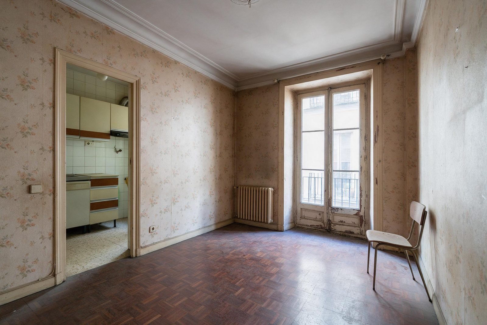 Salón y cocina antiguos de un piso de Madrid antes de la reforma integral, con carpintería y suelos originales